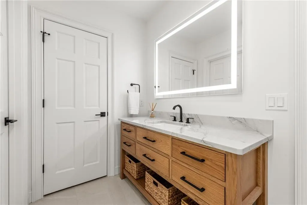Beautiful custom cabinetry is highlighted by quartzite countertops and anti-fog LED mirrors, with a spacious linen closet conveniently tucked behind the door.