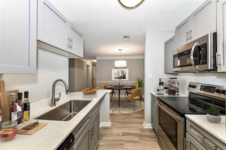 Kitchen with gray cabinetry, stainless steel appliances, hanging light fixtures, light stone countertops, and a textured ceiling