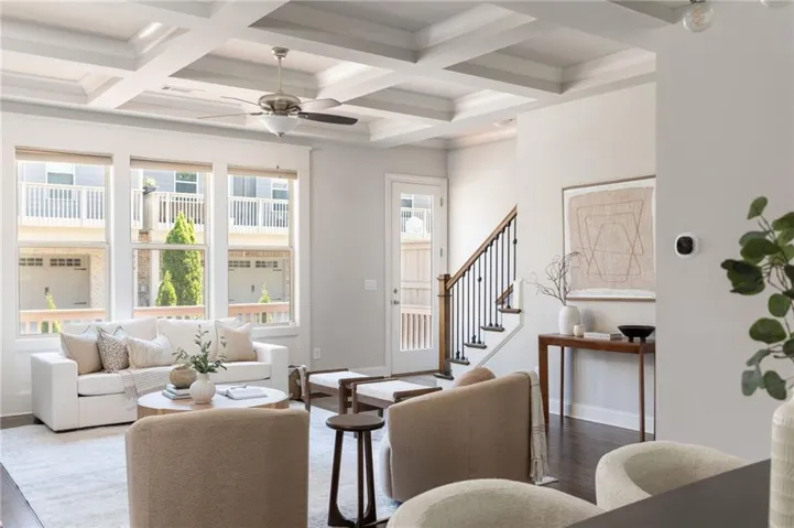 Coffered ceiling with a ceiling fan, multiple tall windows, dark wood-finish flooring, and a staircase with dark wood handrails and black metal balusters