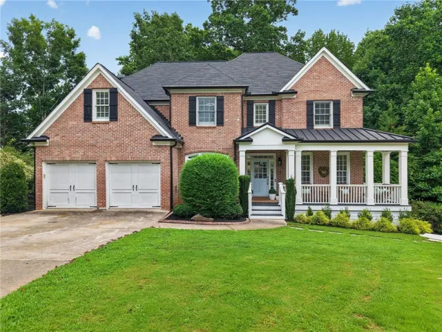 Brick facade residence featuring a covered front porch with white columns, a dark metal roof accent, and a light blue entry door