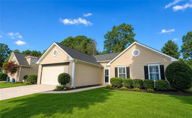Cream-colored siding exterior with a dark shingle roof, contrasting black window shutters, an attached garage, and a manicured lawn with established shrubbery