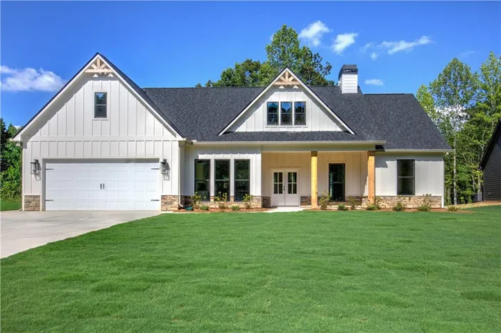 Modern farmhouse-style exterior featuring white board and batten siding, dark shingle roof, stone accents, a two-car garage, and a covered front porch with wood columns