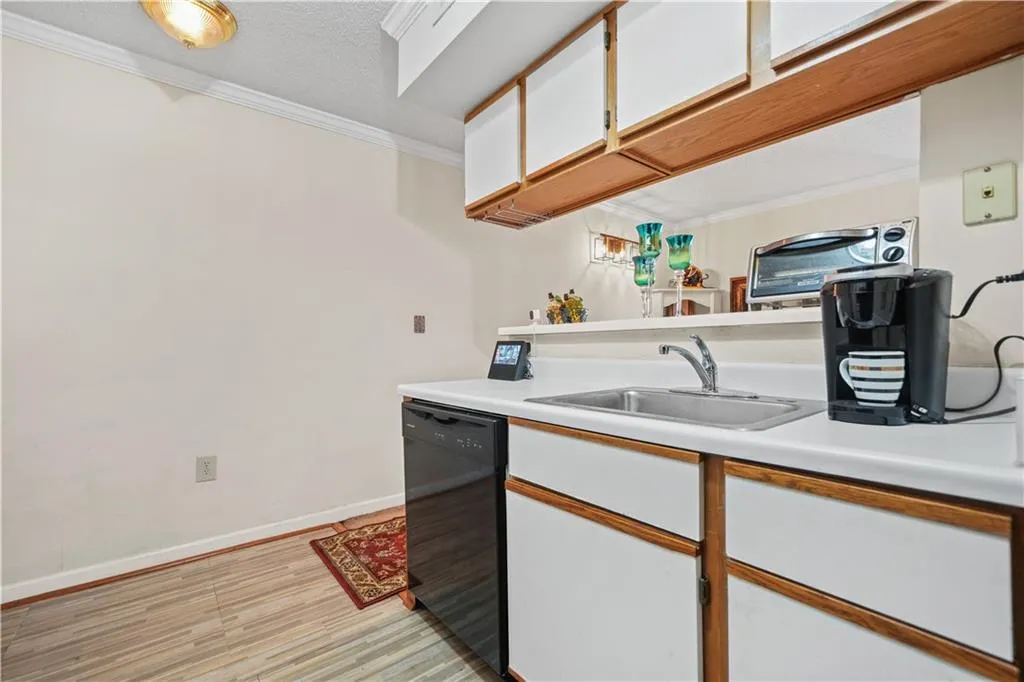 Kitchen with white cabinets, crown molding, light countertops, brown cabinets, and black dishwasher