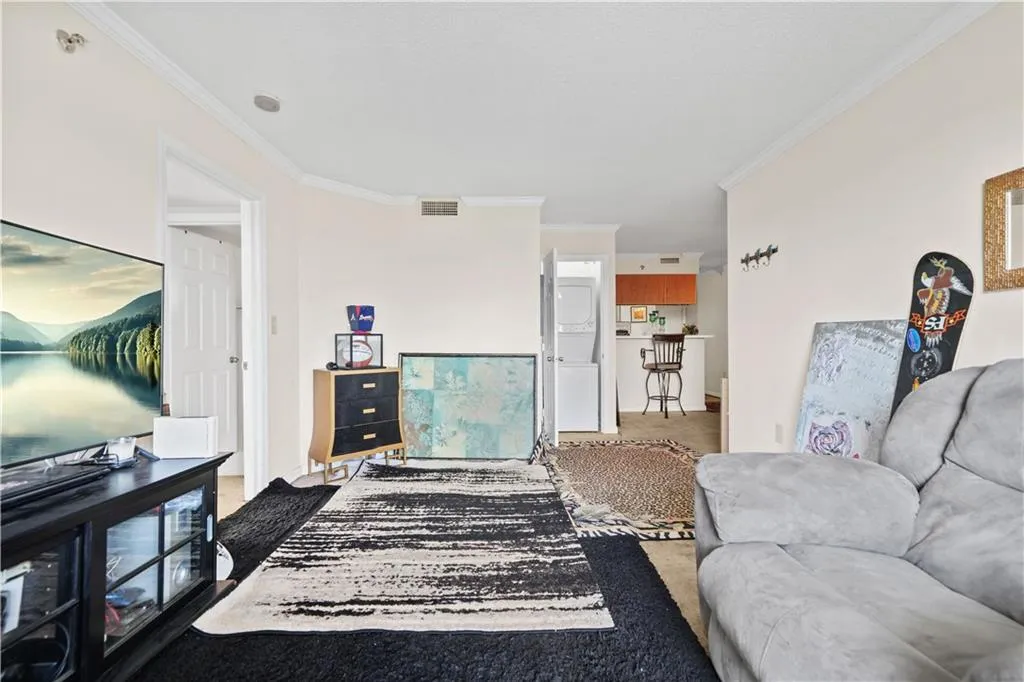 Living area with crown molding, stacked washer and clothes dryer, and carpet floors