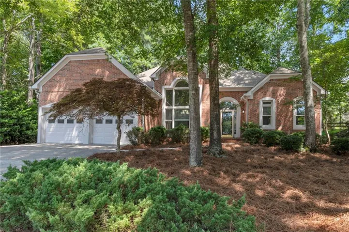 Brick exterior with multiple gables, arched entry, two-car garage, and mature landscaping