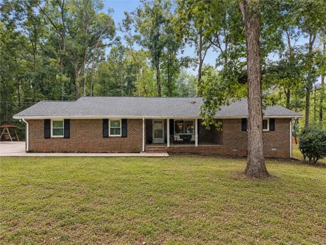 Beautiful four-sides brick home with welcoming front porch on large wooded corner lot.
