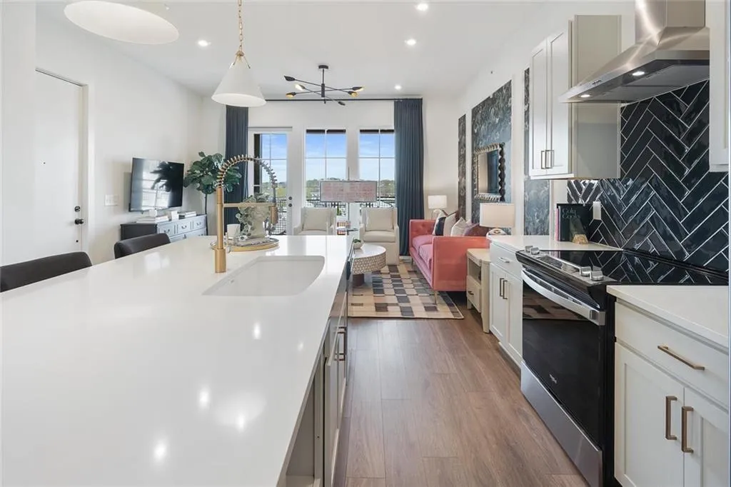 Kitchen featuring wall chimney exhaust hood, stainless steel electric range oven, open floor plan, light countertops, and decorative backsplash