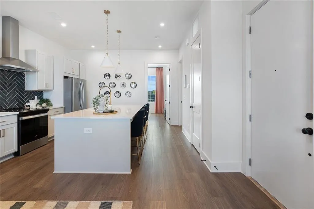 Kitchen with appliances with stainless steel finishes, wall chimney range hood, light countertops, decorative backsplash, and dark wood-type flooring