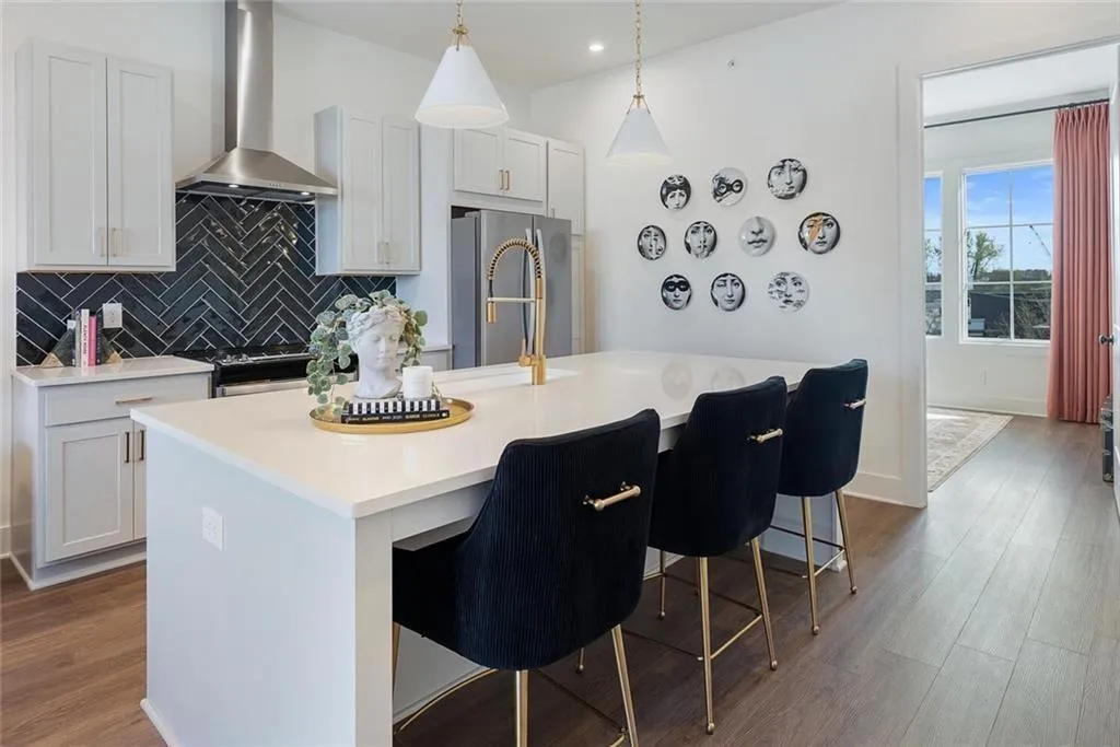 Kitchen featuring wall chimney range hood, freestanding refrigerator, a kitchen island with sink, decorative backsplash, and light countertops