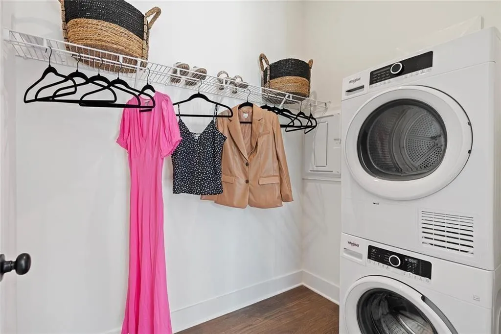 Washroom with stacked washer / drying machine and dark wood-style flooring