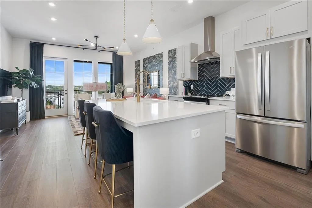 Kitchen with freestanding refrigerator, wall chimney exhaust hood, recessed lighting, an island with sink, and light countertops