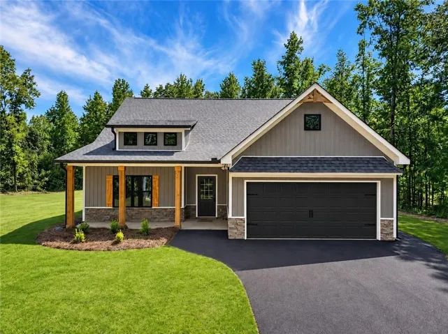 Contemporary single-story exterior featuring a dormer, wood-look shutters, a black garage door, and a stone foundation accent