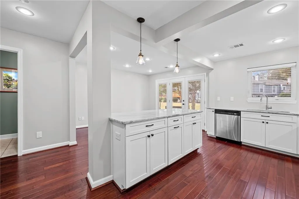Kitchen featuring white cabinetry, beamed ceiling, hanging light fixtures, dark wood-style flooring, and light stone counters
