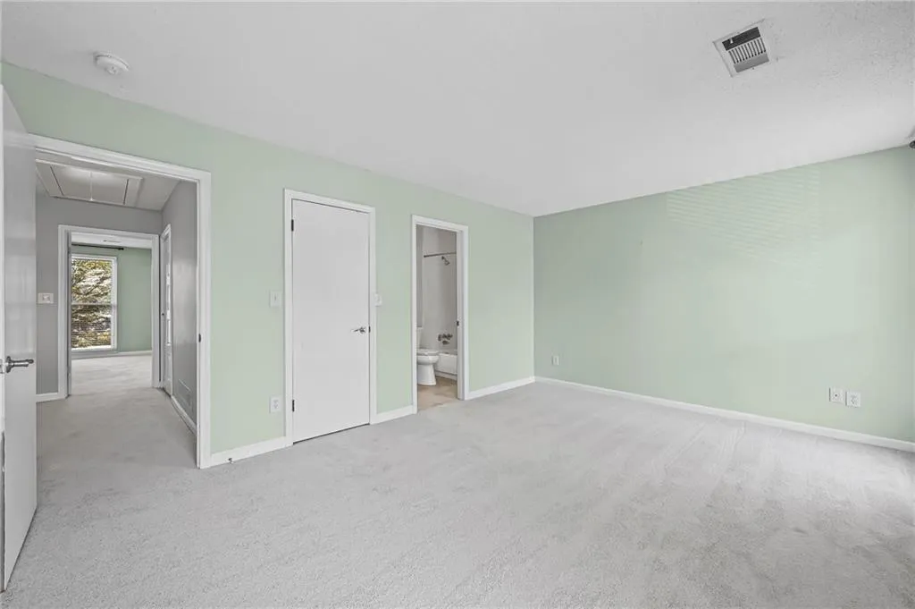 Unfurnished bedroom featuring attic access, light carpet, a closet, and ensuite bath