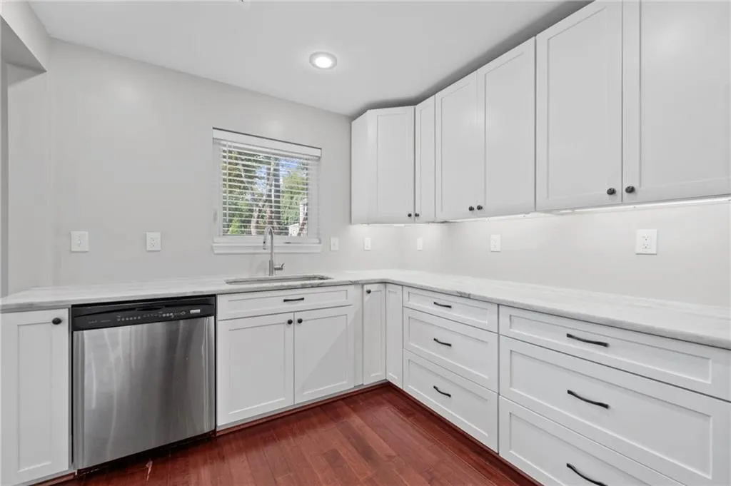Kitchen with white cabinetry, stainless steel dishwasher, dark wood finished floors, and light stone countertops
