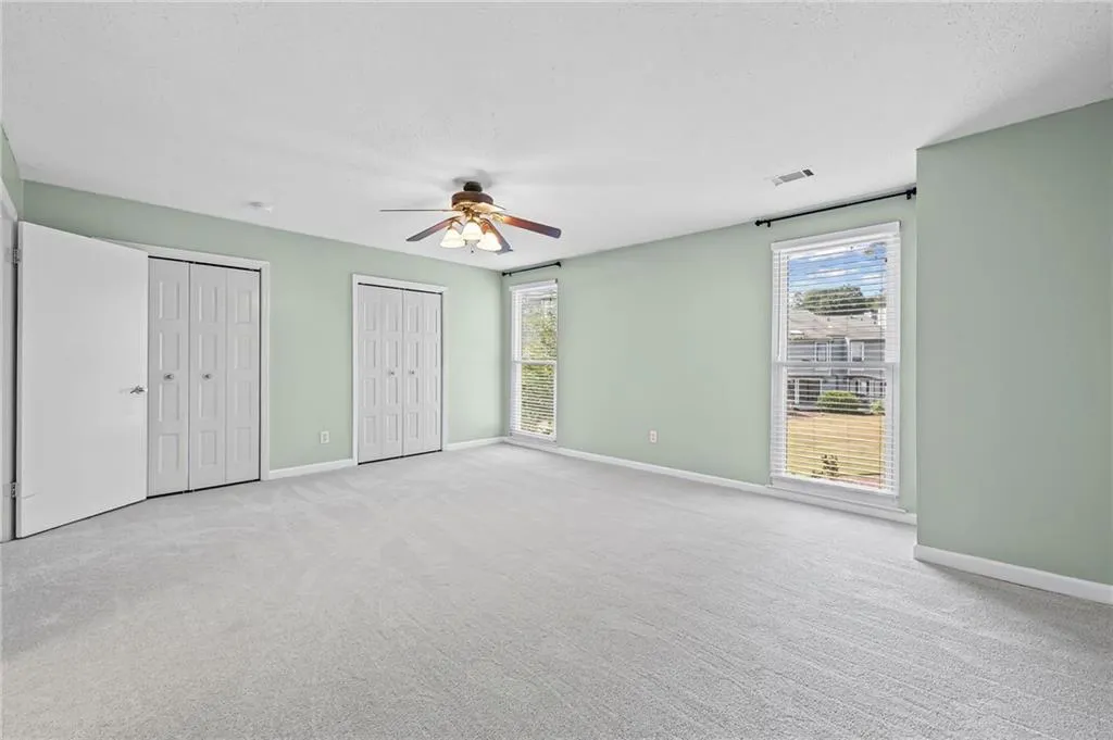 Unfurnished bedroom featuring multiple closets, light carpet, ceiling fan, and a textured ceiling