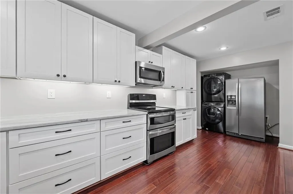 Kitchen with appliances with stainless steel finishes, white cabinets, dark wood-style floors, estacked washer and dryer, and recessed lighting