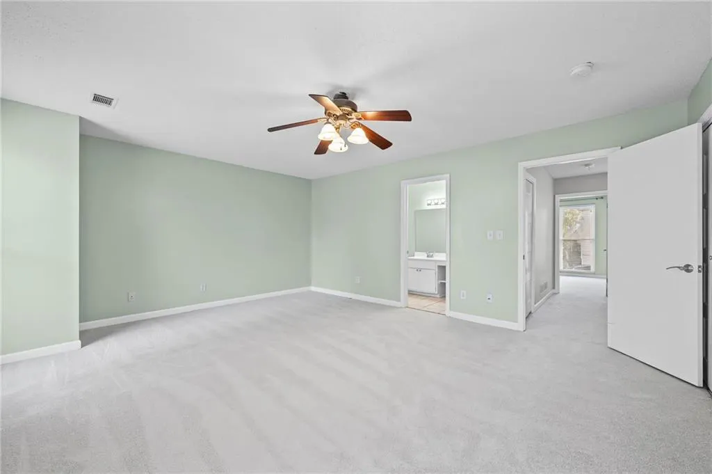 Unfurnished bedroom with light colored carpet, ceiling fan, and ensuite bath