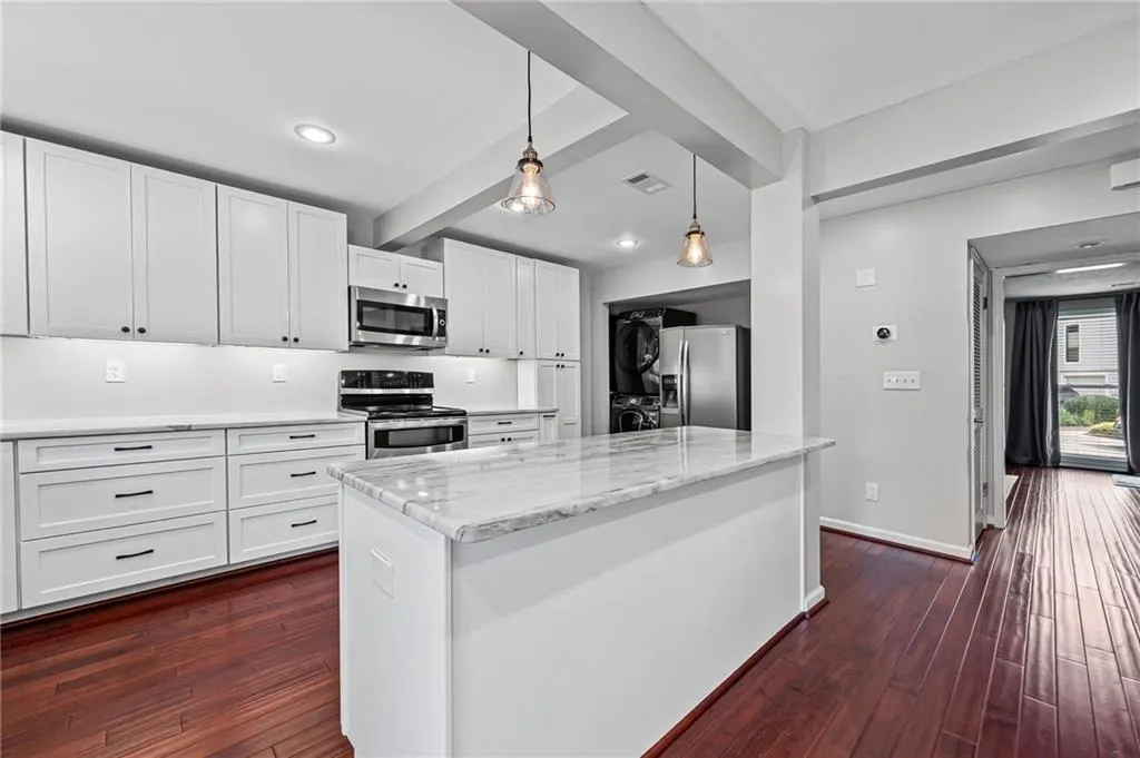 Kitchen with beamed ceiling, decorative light fixtures, dark wood-style floors, white cabinets, and stainless steel appliances