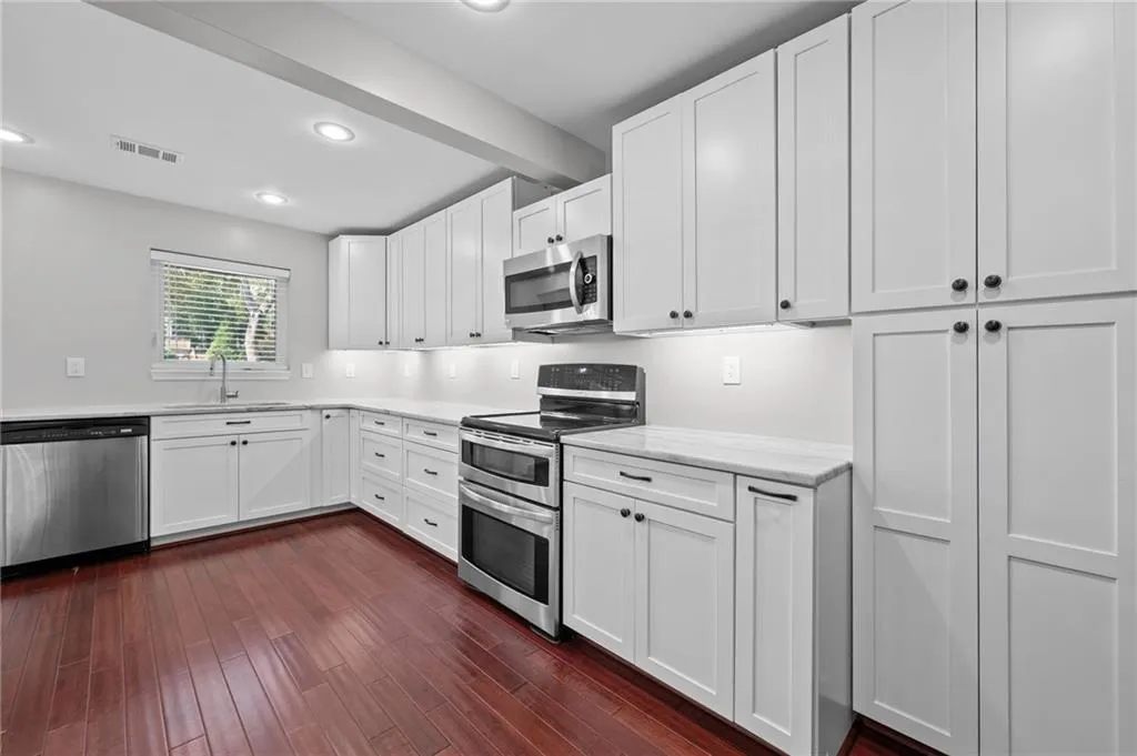 Kitchen with stainless steel appliances, white cabinetry, dark wood finished floors, beam ceiling, and recessed lighting