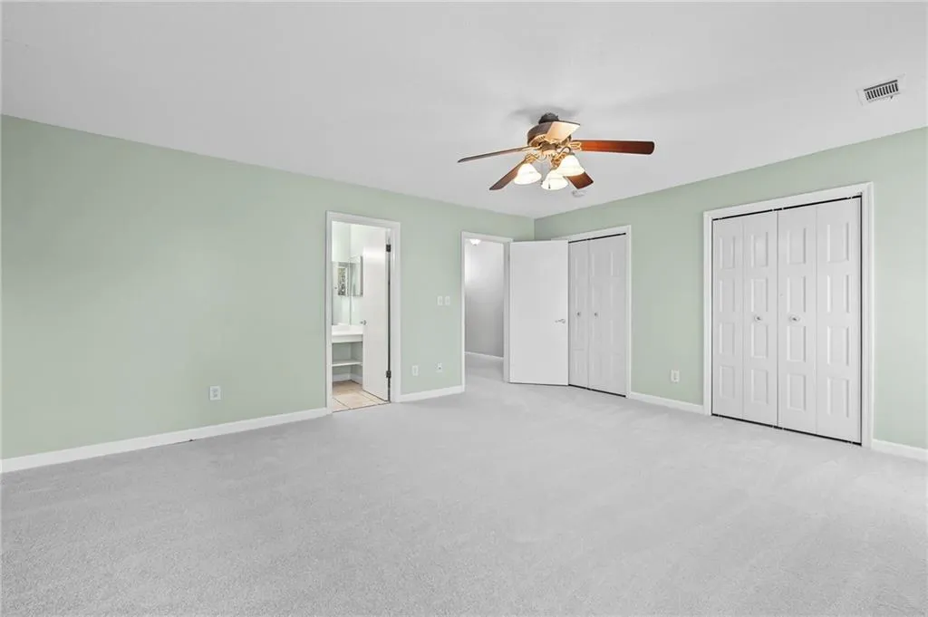 Unfurnished bedroom with two closets, light carpet, ensuite bathroom, and a ceiling fan