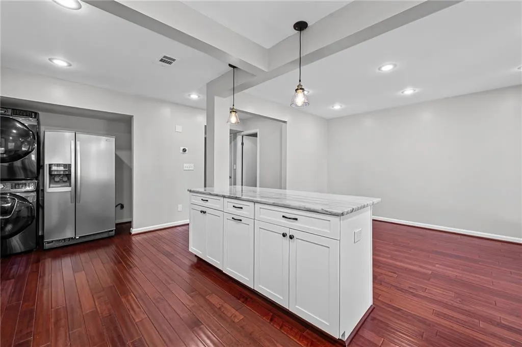 Kitchen featuring stainless steel fridge with ice dispenser, white cabinetry, a kitchen island, dark wood-style floors, and pendant lighting