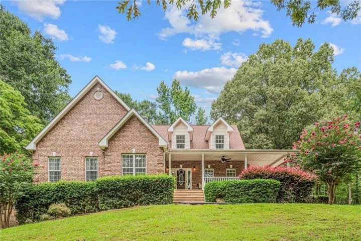 Brick facade residence featuring a covered front porch with white railing, dormer windows, and mature landscaping