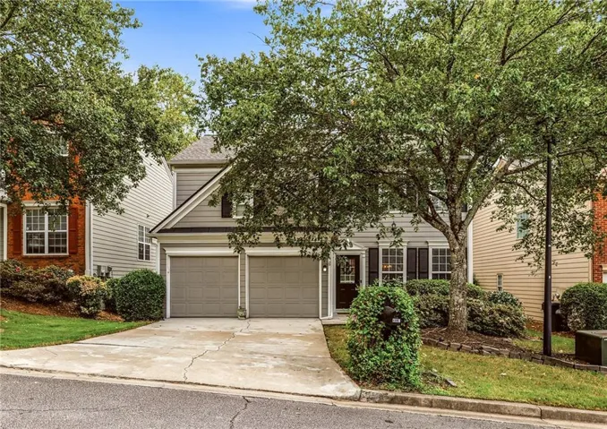 Two-story residence featuring a two-car garage, front entry with transom window, and mature landscaping