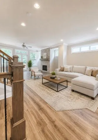 Open-concept living space anchored by a wood-finish plank floor throughout, recessed ceiling lighting, and a fireplace with stone surround