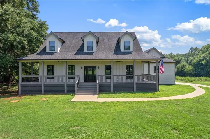 Farmhouse-style exterior featuring a covered porch, dormer windows, dark-frame windows, a paved walkway, and a manicured lawn