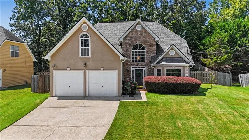 Stucco and stone facade with a gray shingle roof, arched windows, and a two-car garage