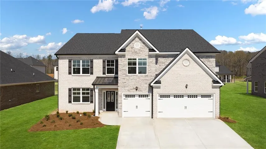 Contemporary residence featuring a light brick and stone facade, dark shingle roof, dark paneled shutters, a covered entry, and a two-car garage