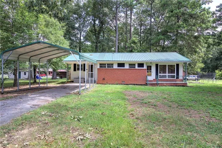 Charming brick residence featuring a metal roof, multiple windows with natural light, and a covered carport