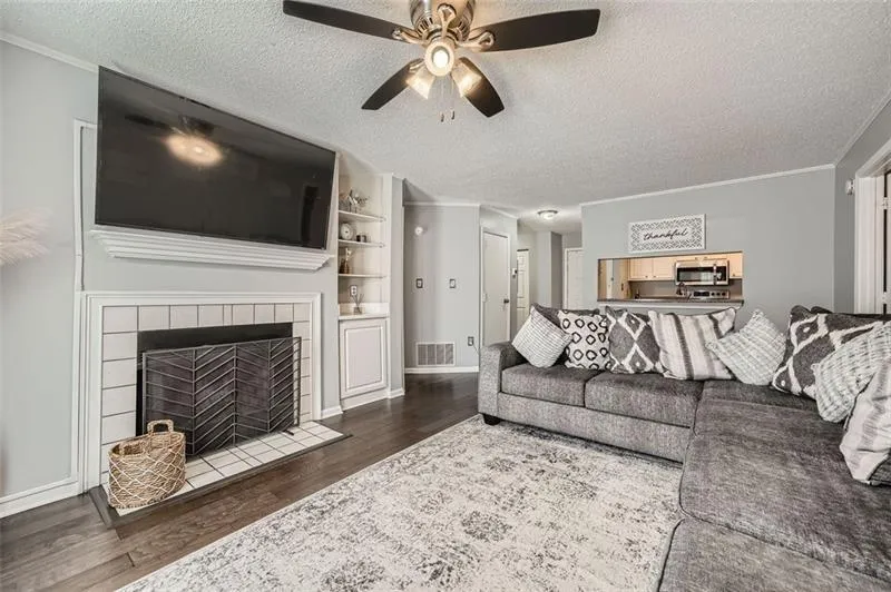 Living area with a textured ceiling, dark wood-type flooring, crown molding, built in shelves, and ceiling fan