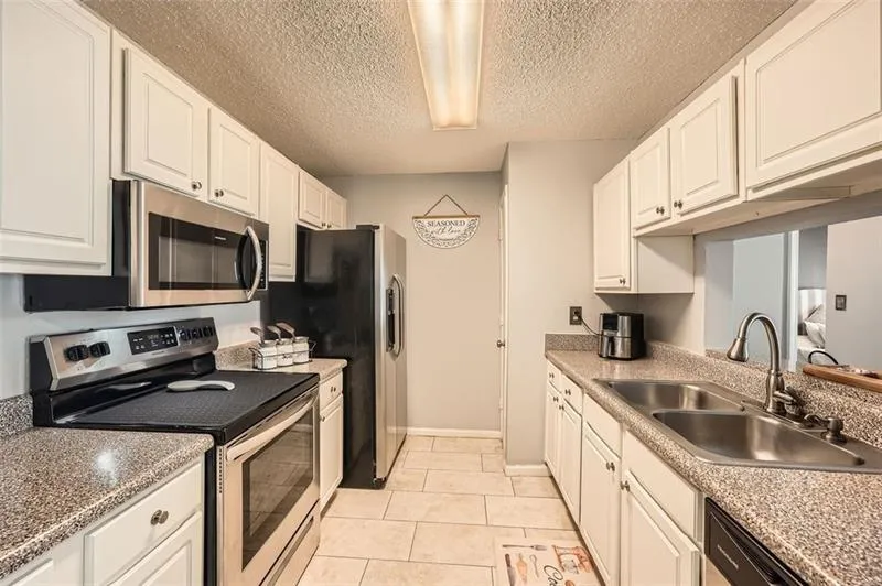 Kitchen featuring stainless steel appliances, a textured ceiling, white cabinets, and light tile patterned flooring