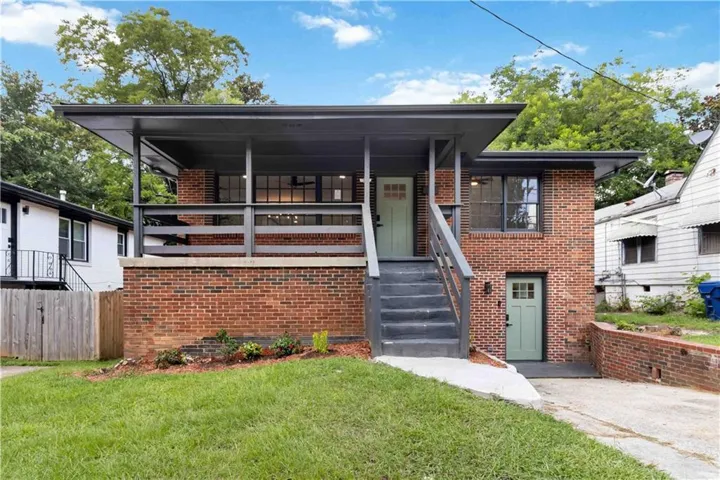 Brick exterior residence featuring a covered front porch with dark railings and a light green entry door