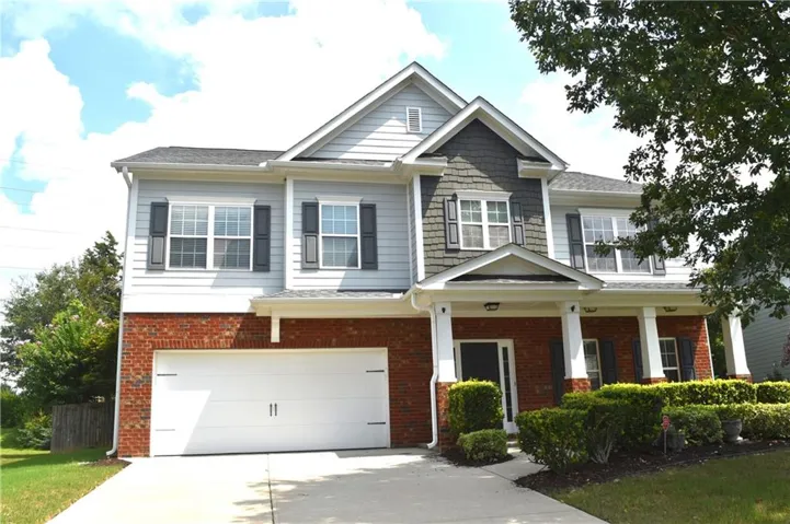 Multi-level facade with brick and siding, covered front porch with pillars, attached two-car garage, and established front landscaping