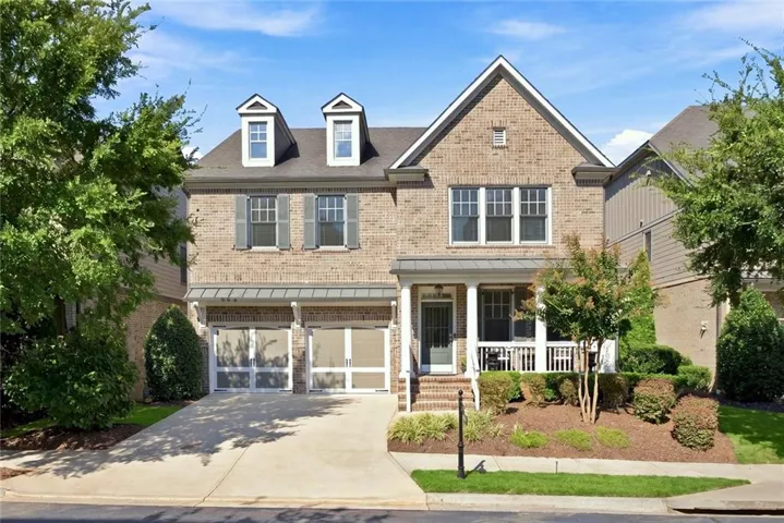 Brick exterior with multiple gables, covered front porch, dormer windows, and a two-car garage with frosted-panel doors