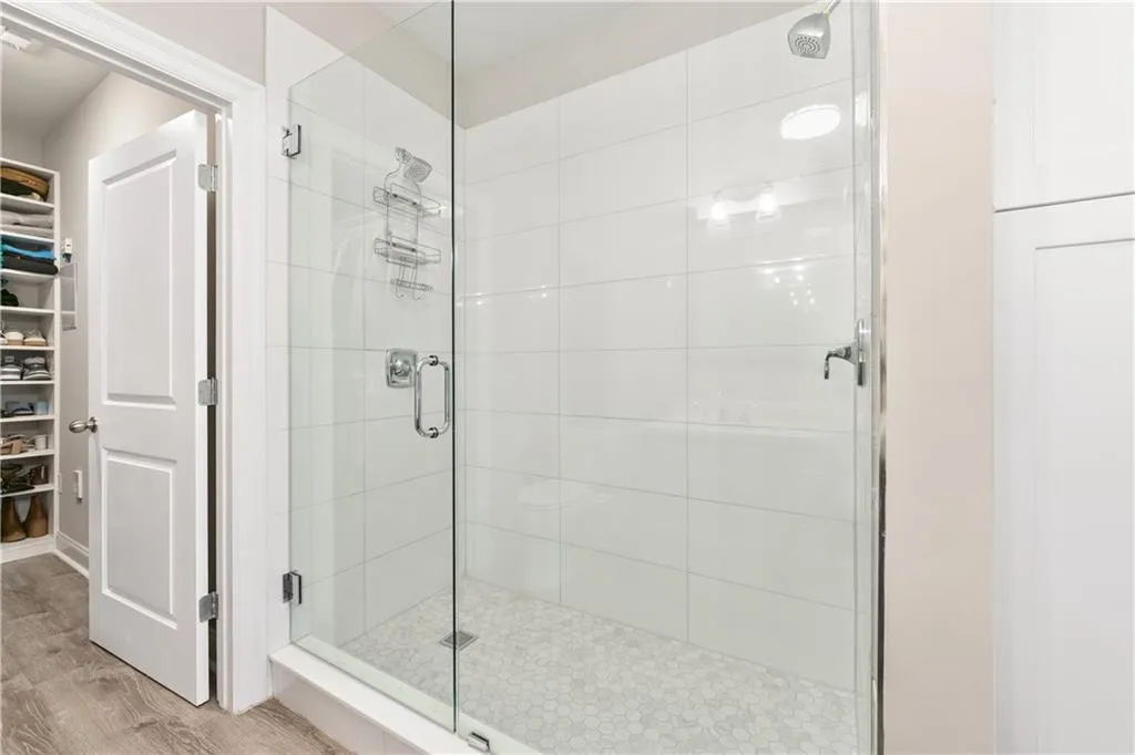 Full bathroom with a spacious closet, a shower stall, and wood finished floors