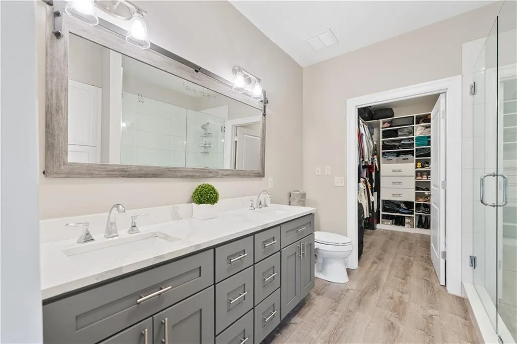 Full bath featuring a shower stall, double vanity, a walk in closet, and light wood-style floors