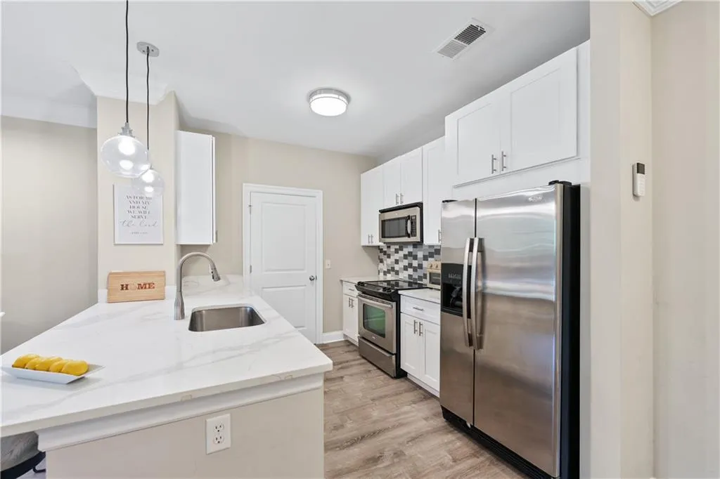 Kitchen featuring appliances with stainless steel finishes, decorative backsplash, light stone counters, and white cabinetry