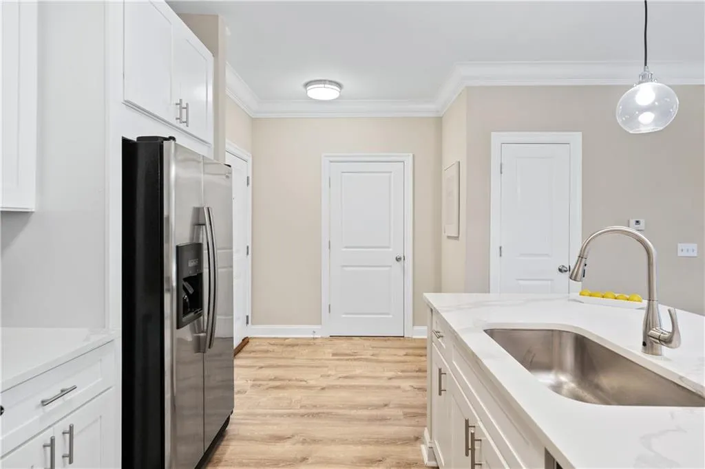 Kitchen with white cabinetry, stainless steel fridge with ice dispenser, ornamental molding, light wood-style flooring, and pendant lighting