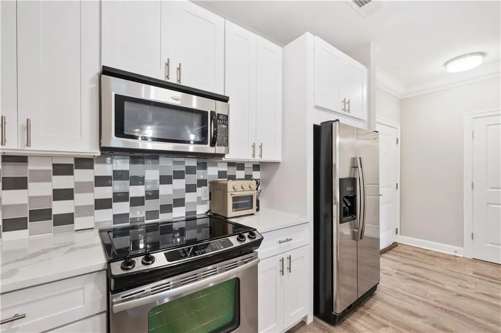 Kitchen featuring appliances with stainless steel finishes, backsplash, ornamental molding, white cabinetry, and light wood finished floors