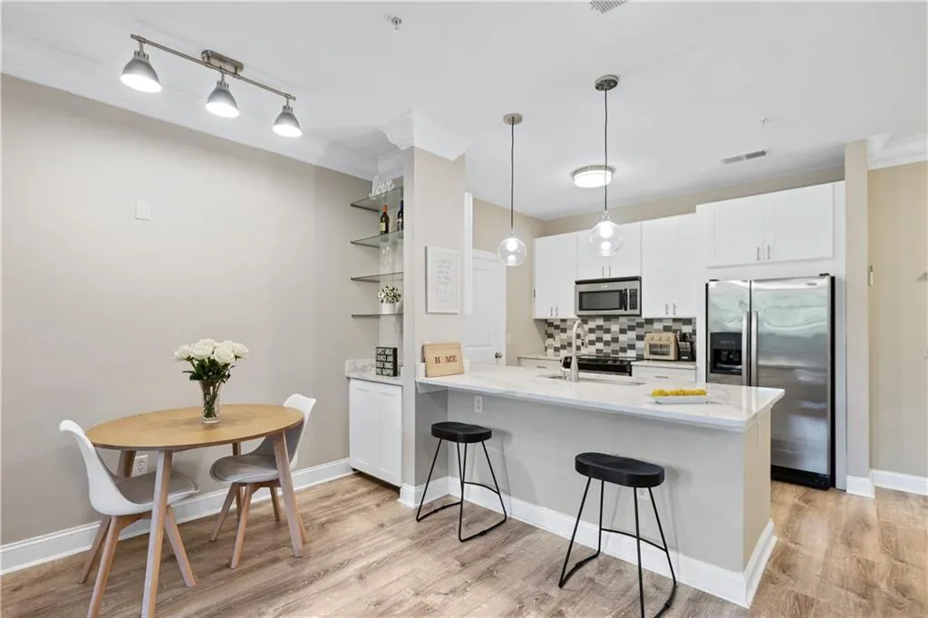 Kitchen featuring appliances with stainless steel finishes, white cabinetry, tasteful backsplash, hanging light fixtures, and a breakfast bar
