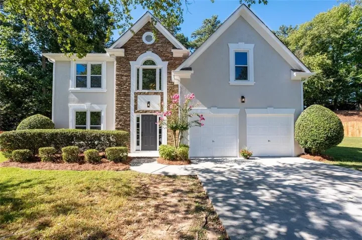 Stucco and stone facade with arched and rectangular window designs, a two-car garage, and a concrete driveway