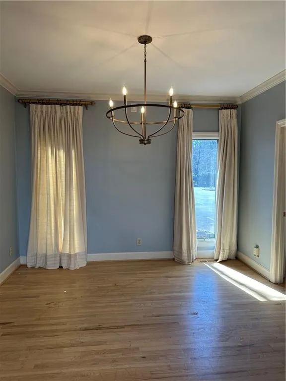 Unfurnished room with a notable chandelier, crown molding, baseboards, and wood finished floors