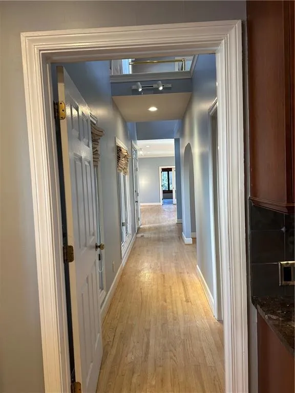 Hallway featuring baseboards, arched walkways, and light wood finished floors