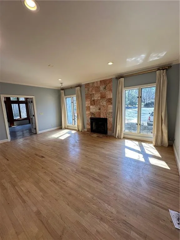 Unfurnished living room featuring wood finished floors, recessed lighting, crown molding, a premium fireplace, and baseboards