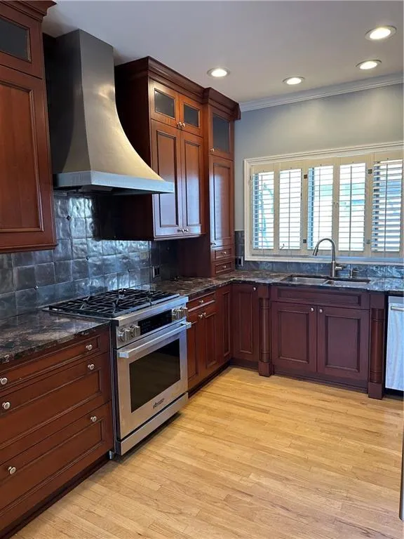 Kitchen featuring ventilation hood, light wood-style flooring, ornamental molding, a sink, and stove