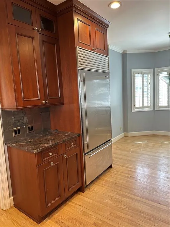 Kitchen with light wood finished floors, baseboards, ornamental molding, decorative backsplash, and freestanding refrigerator